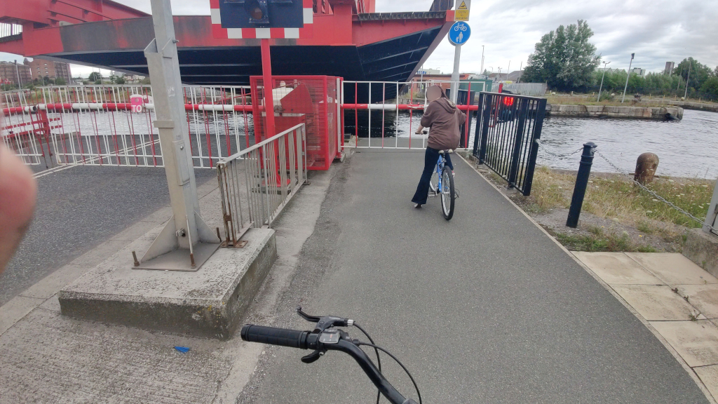 view from a bicycle of a rising red road bridge over dockland