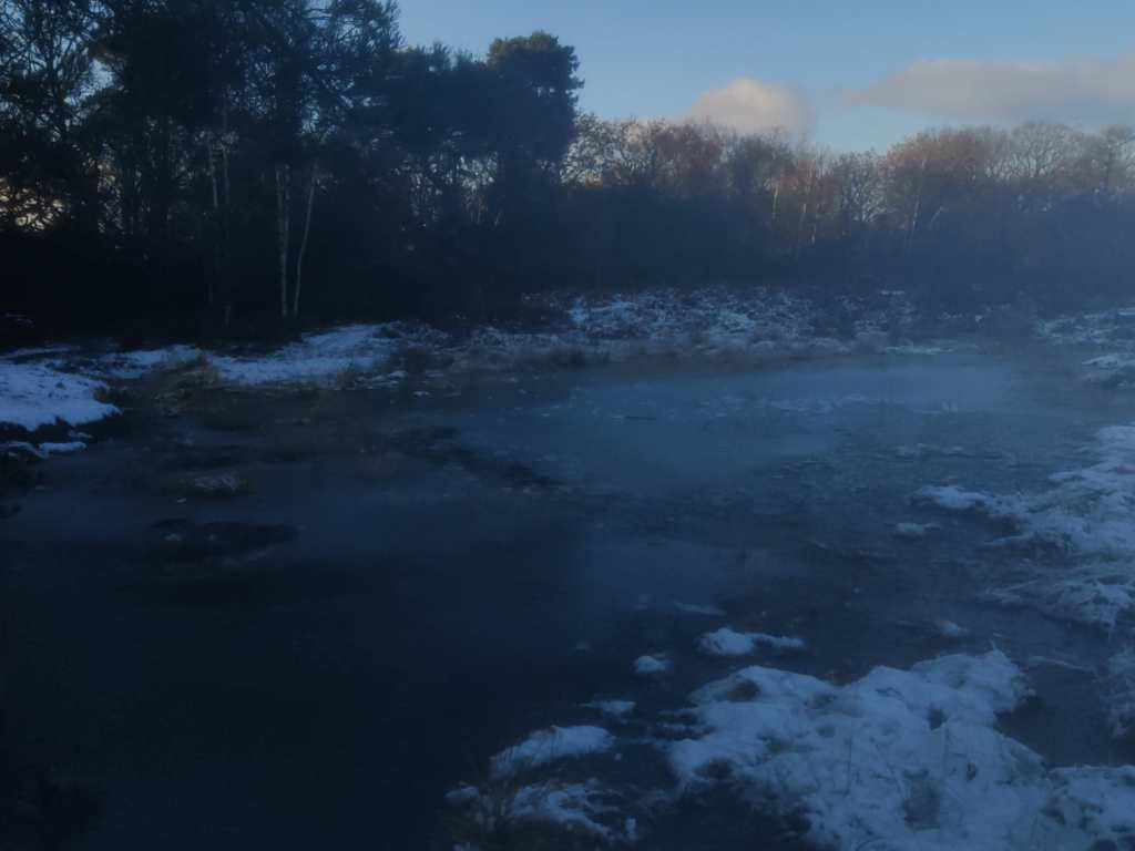 A photo of a frozen pond, surrounded by frozen snow