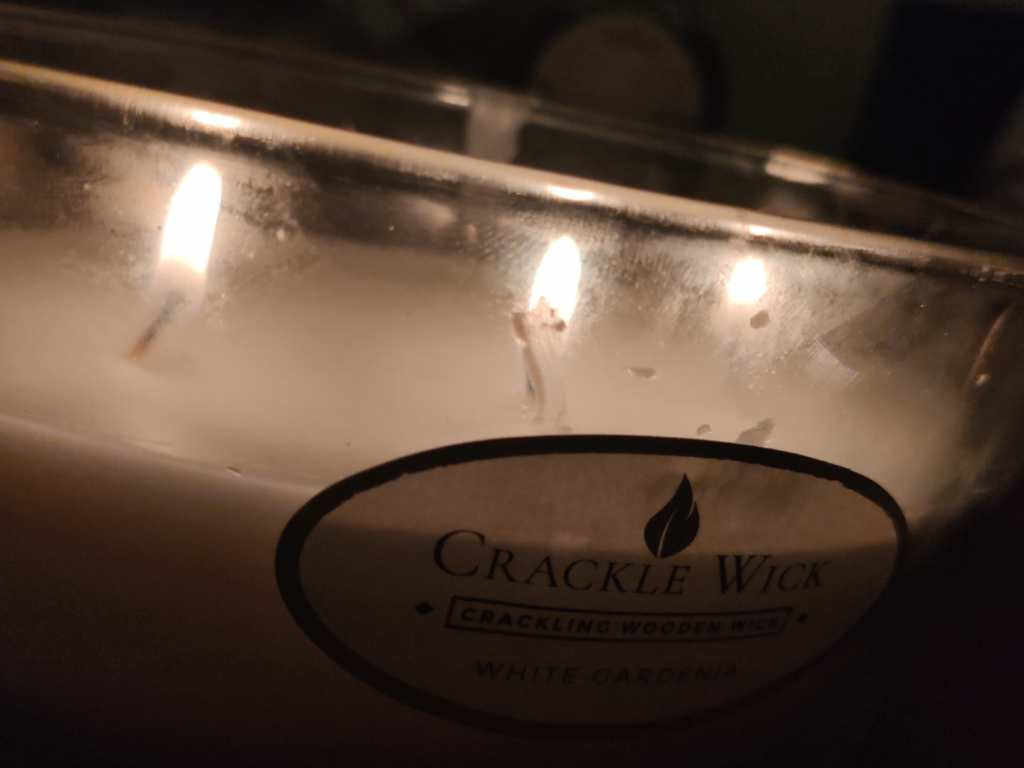 A photo of a lit three wick crackle wick candle, with household string instead of wood