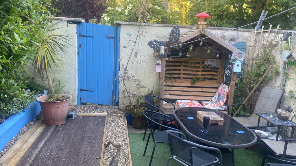 A back yard - featuring a deck, an arbour, and a low glass-topped table